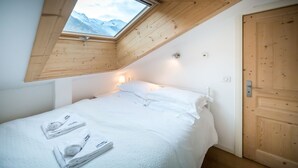 A bedroom with a skylight, a bed with white linens, and a wooden door. - Rupicapra apartment -  an apartment that sleeps 6 guests  in 3 bedrooms (Chamonix)
