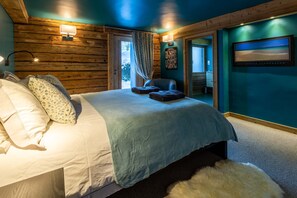 A bedroom with a wooden headboard, a bed with white linens, a blue throw blanket, and a fluffy rug.