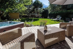 Une terrasse dotée de meubles en osier, d’un jacuzzi et d’une pelouse verdoyante offrant une vue sur les montagnes.