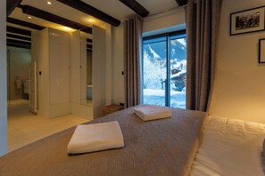 Une chambre dotée d’un grand lit, d’un dressing et offrant une vue sur un paysage enneigé grâce à une porte vitrée.