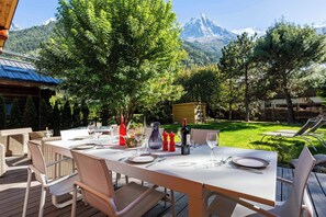 Un espace de restauration en plein air avec une table dressée pour deux personnes, entourée de chaises, et une vue sur les montagnes en arrière-plan.
