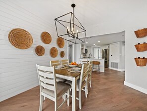 A modern kitchen with white cabinetry, a central island, and a dining area with a wooden table and chairs. - Breathtaking 4th Floor Ocean Views (Hilton Head Island)