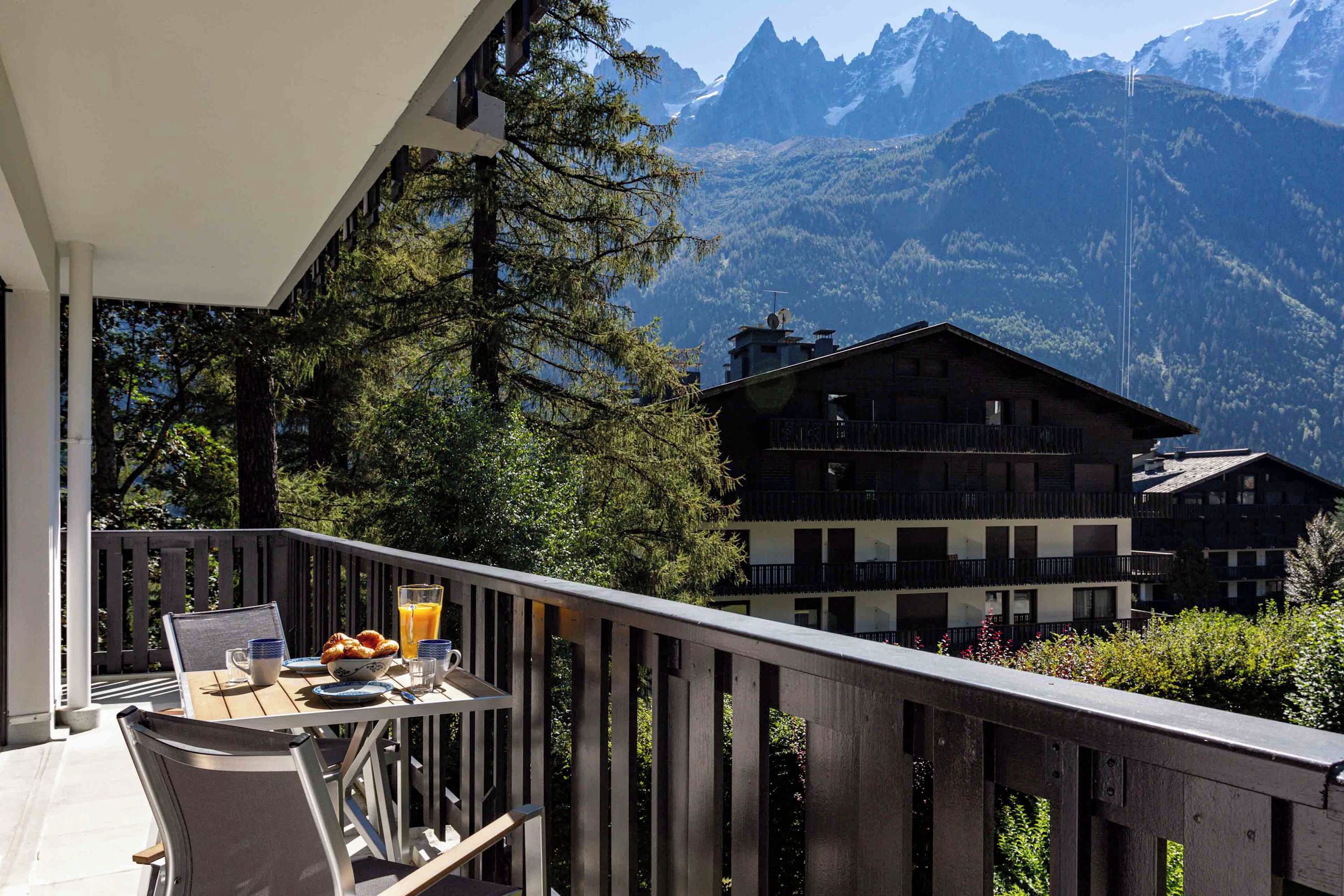 Een balkon met een ontbijtje erop, met uitzicht op een berglandschap en gebouwen in chaletstijl.