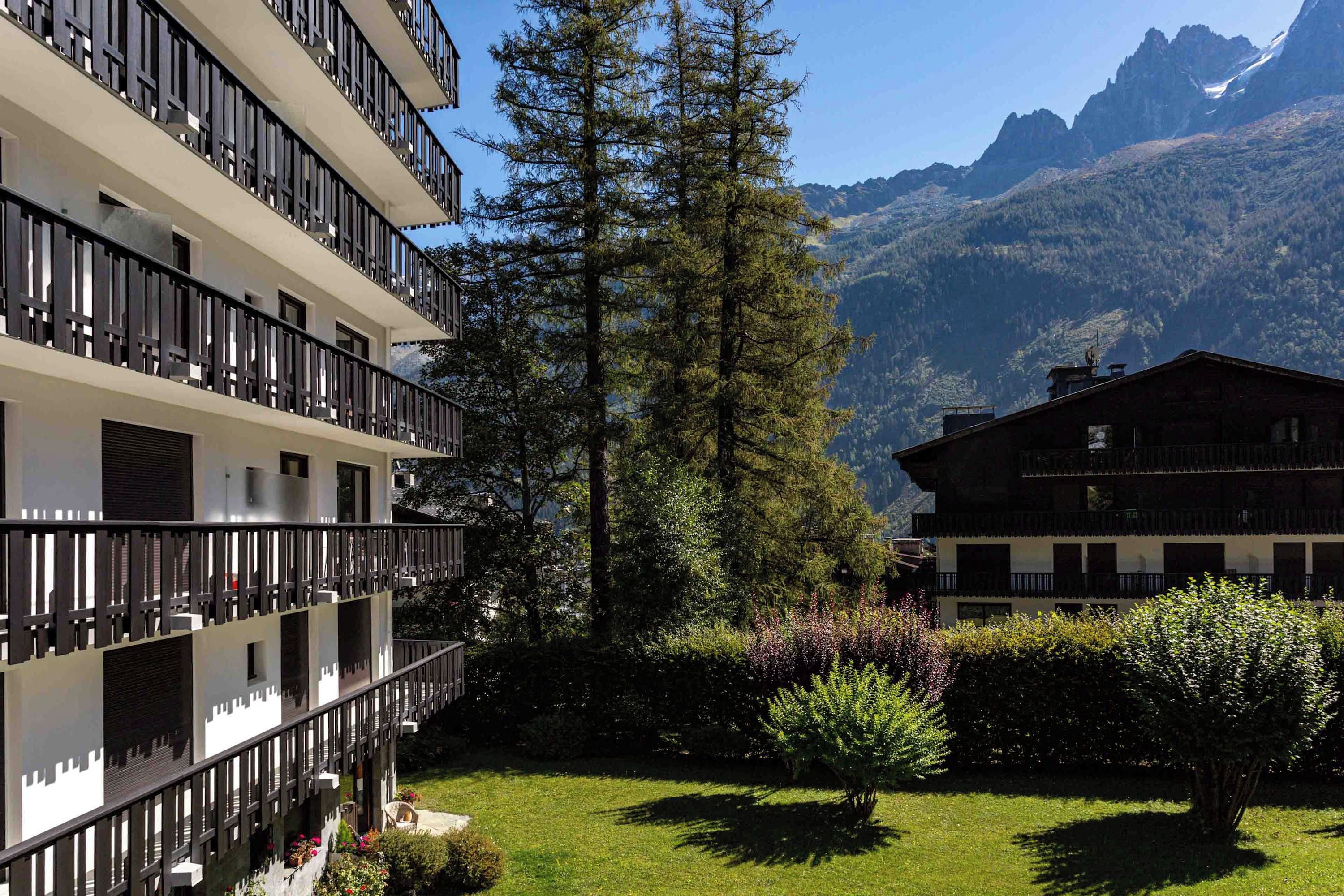 Un immeuble à plusieurs étages, doté de balcons, entouré de verdure et avec des montagnes en arrière-plan.