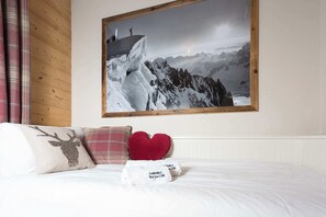 Een slaapkamer met een bed, kussens, een lijst met een foto van een berglandschap en een houten wandpaneel.