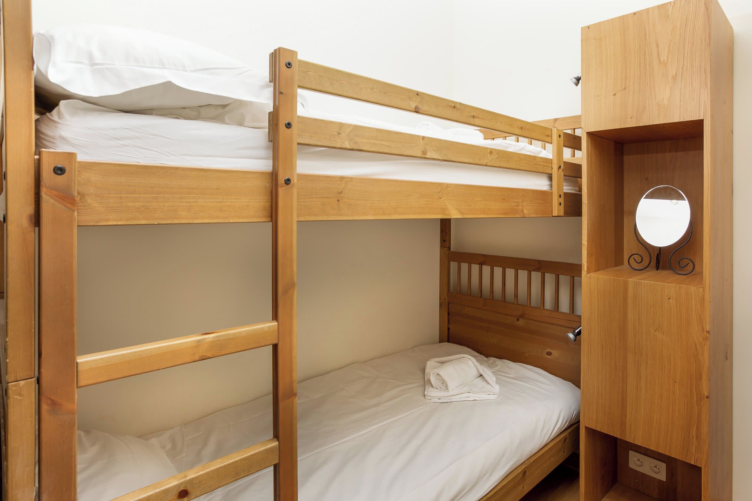 Een stapelbed met houten frame en een klein houten kastje met spiegel.