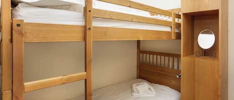 Una cama individual sobre otra con estructura de madera y un pequeño mueble de madera con espejo.