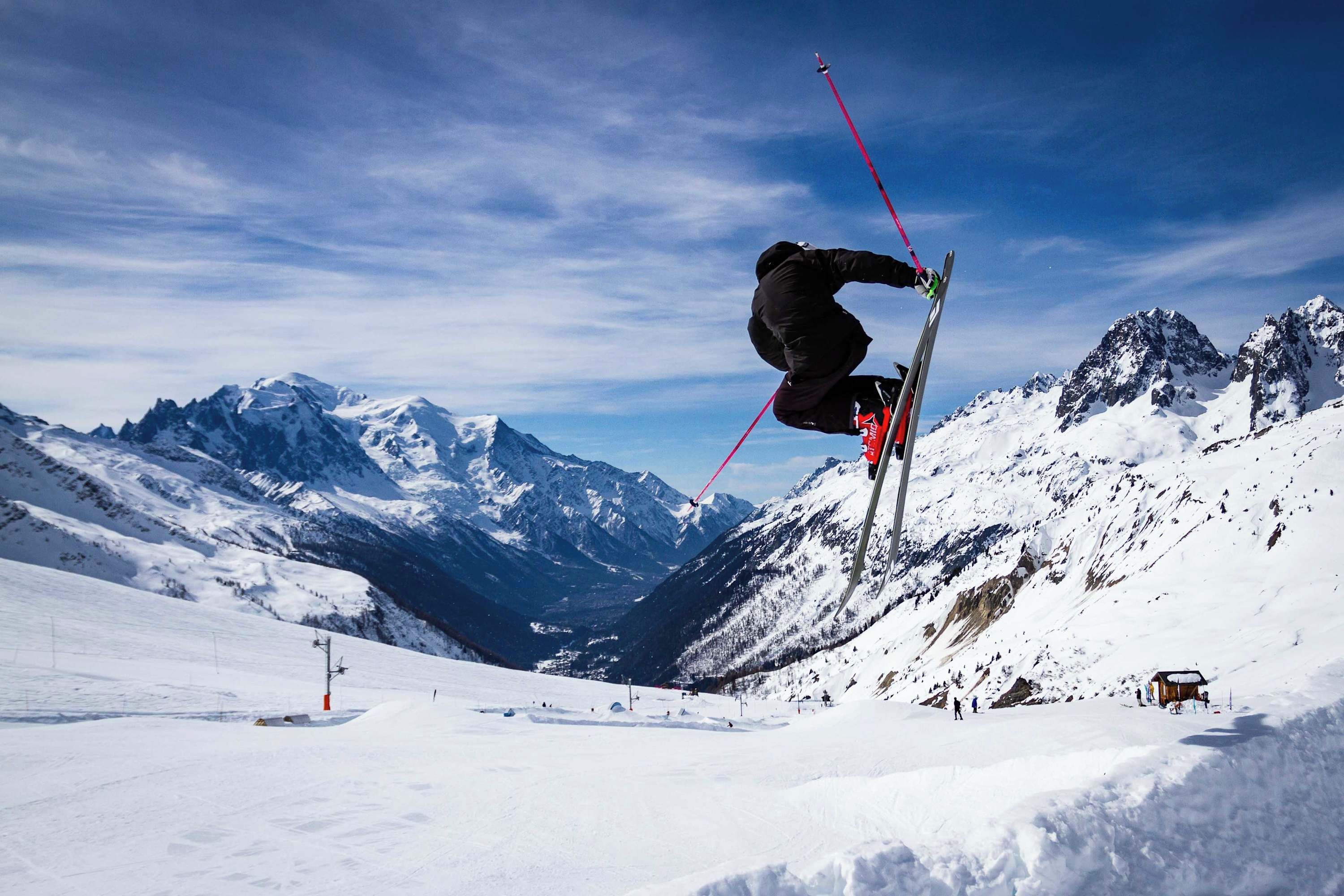 A skier performing a jump with a mountainous backdrop.
