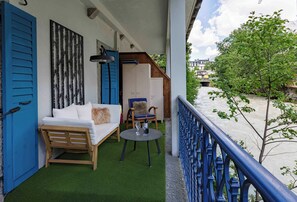 A balcony with a sofa, chairs, and a table, overlooking a river and buildings.