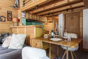 A cozy wooden cabin interior with a dining area, a kitchenette, and a sofa.