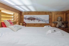 A hotel room with a bed, pillows, a teddy bear, a painting, and a statue.