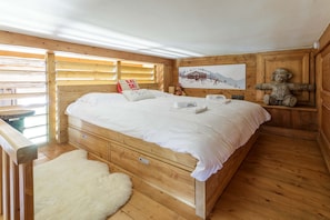 A wooden cabin-style bedroom with a bed, a fluffy rug, a ski-themed sign, and a mountain painting.