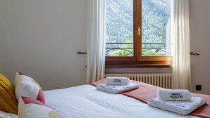 Hotellihuone, jossa on sänky, tyynyt, vuoristonäkymällä varustettu ikkuna ja logolla varustetut pyyhkeet.