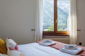 A hotel room with a bed, pillows, a window with a mountain view, and towels with a logo.