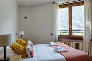 A hotel room with a bed, a bedside lamp, a window with curtains, and a view of a forest.