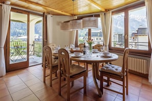 A dining area with a round table, chairs, and a view of mountains through large windows. - Residence des Alpes 302, Skiing, Chamonix All year (Chamonix)