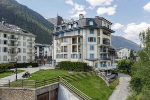 Un hotel de varios pisos con balcones, un patio empedrado y montañas al fondo.