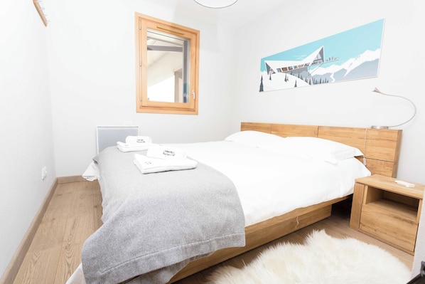 Une chambre à coucher avec un lit en bois, une table de chevet, une commode, un miroir, un radiateur et un tableau accroché au mur.