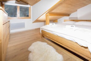 A bedroom with a sloped ceiling, wooden bed frame, white bedding, a fluffy rug, and a window with a view.
