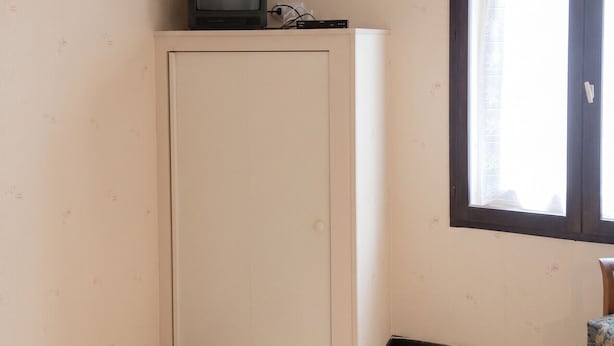 Habitación con armario, televisor encima, ventana con cortinas y una silla.