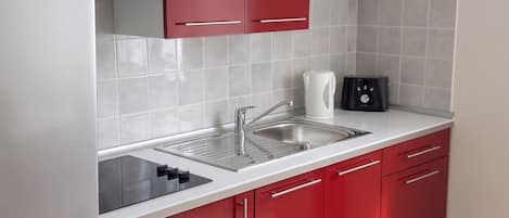 Una cocina con gabinetes rojos, un lavamanos de acero inoxidable, un microondas y una cafetera.