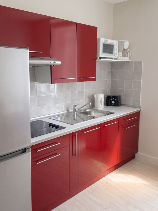 A kitchen with red cabinets, a stainless steel sink, a microwave, and a coffee maker.