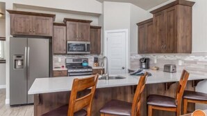 Eine moderne Küche mit Holzschränken, einem Edelstahlkühlschrank, einer Mikrowelle und einer großen Kochinsel mit Barhocker.