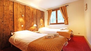 A hotel room with two beds, wooden paneling on one wall, a window with curtains, and a red carpet.