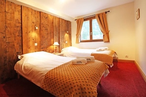 A hotel room with two beds, wooden paneling on one wall, a window with curtains, and a red carpet.
