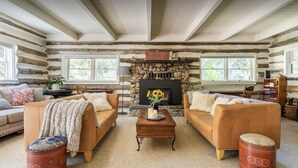 Ein gemütliches Blockhaus-Interieur mit zwei Sofas, einem Couchtisch, einem Kamin aus Stein und einem Bücherregal.