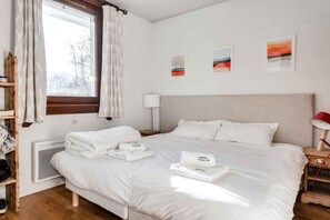A hotel room with a bed, a window with curtains, a bedside table with a lamp, and artwork on the wall.