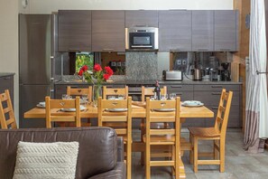 Une cuisine moderne avec un coin repas, comprenant un îlot central agrémenté d’un vase de roses rouges, des chaises en bois et un canapé en cuir.
