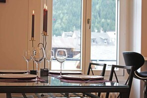 A dining table set with plates, glasses, and candles, with a view of buildings through a window.