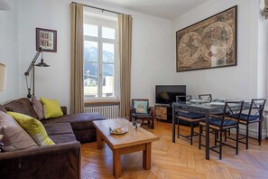 A living room with a sofa, a wooden coffee table, a dining table with chairs, a television, and a large world map on the wall.