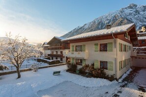 Een meerlaags chalet met een balkon, omgeven door met sneeuw bedekte bergen.