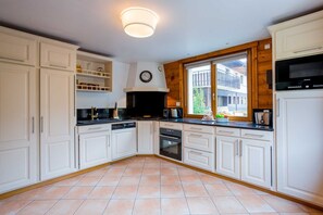 Een keuken met witte kasten, een zwart fornuis en een raam met uitzicht op een gebouw.