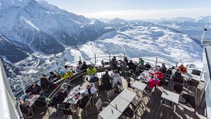 A restaurant with outdoor seating overlooking snow-covered mountains.
