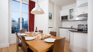 A dining area with a wooden table set for six, a red curtain, and a city view through large windows.