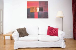 A white sofa with two cushions, a lamp, and a painting on the wall. - Historical Mont Blanc 98 Apt - Chamonix All Year (Chamonix)