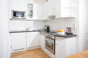 Een moderne keuken met witte kastjes, een ingebouwde magnetron, een broodrooster en een blender op het aanrecht.