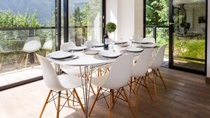 Un comedor moderno con una mesa grande dispuesta para seis personas, rodeada de sillas blancas con patas de madera.