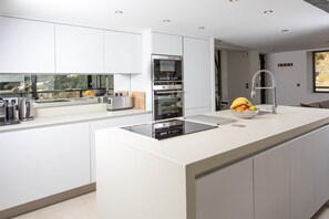 Une cuisine moderne avec des meubles blancs, un îlot central agrémenté d’un panier de fruits et des appareils électroménagers intégrés.