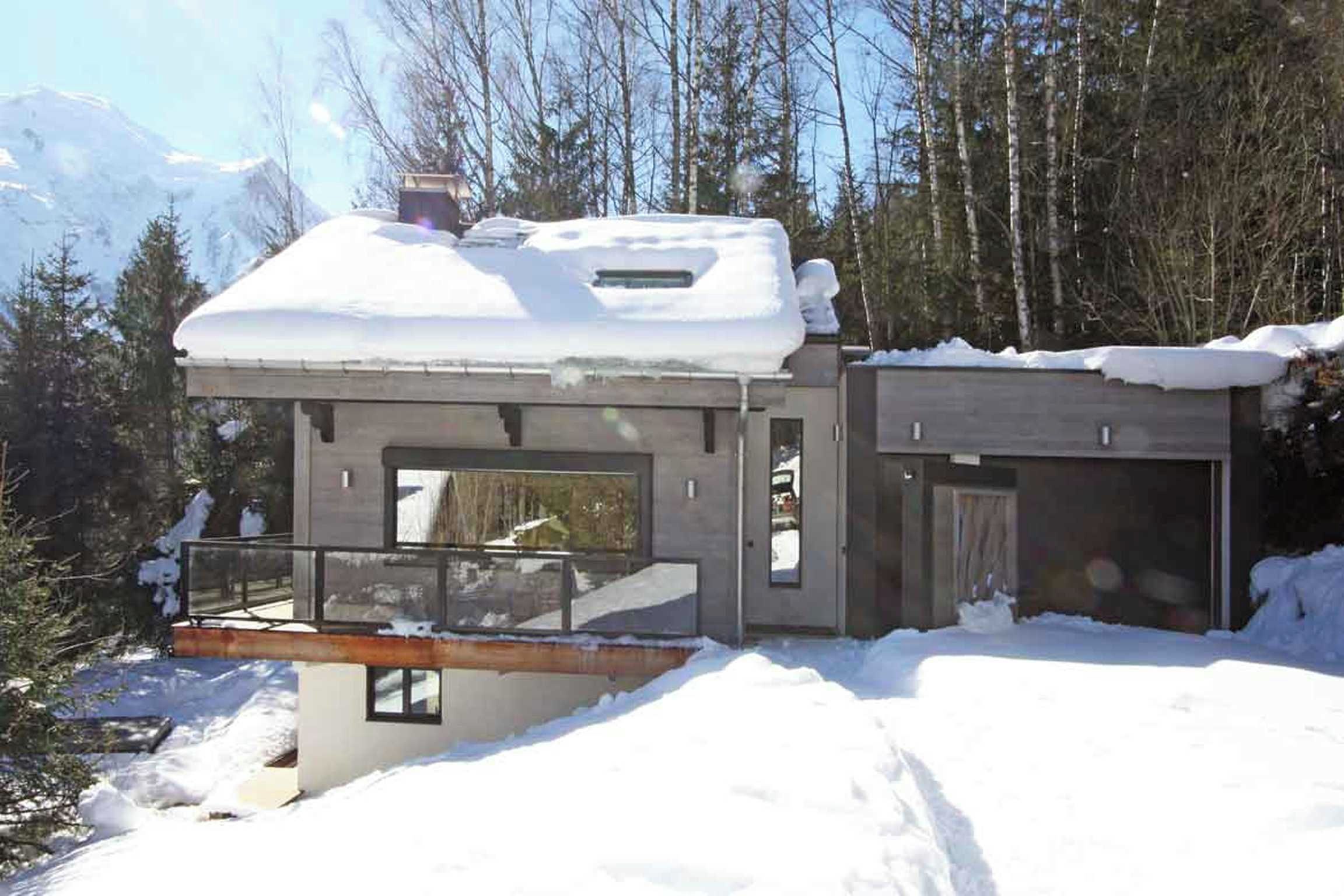 Una casa moderna con tejado nevado, ventanas amplias y un balcón.
