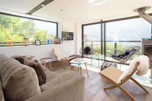 A modern living room with a sofa, chairs, a small table, and a balcony with a view. - Ski Chalet La Source with hot tub (Chamonix)