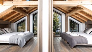 Reflejo de un dormitorio con vigas de madera, ventanas amplias y una cama con toallas.