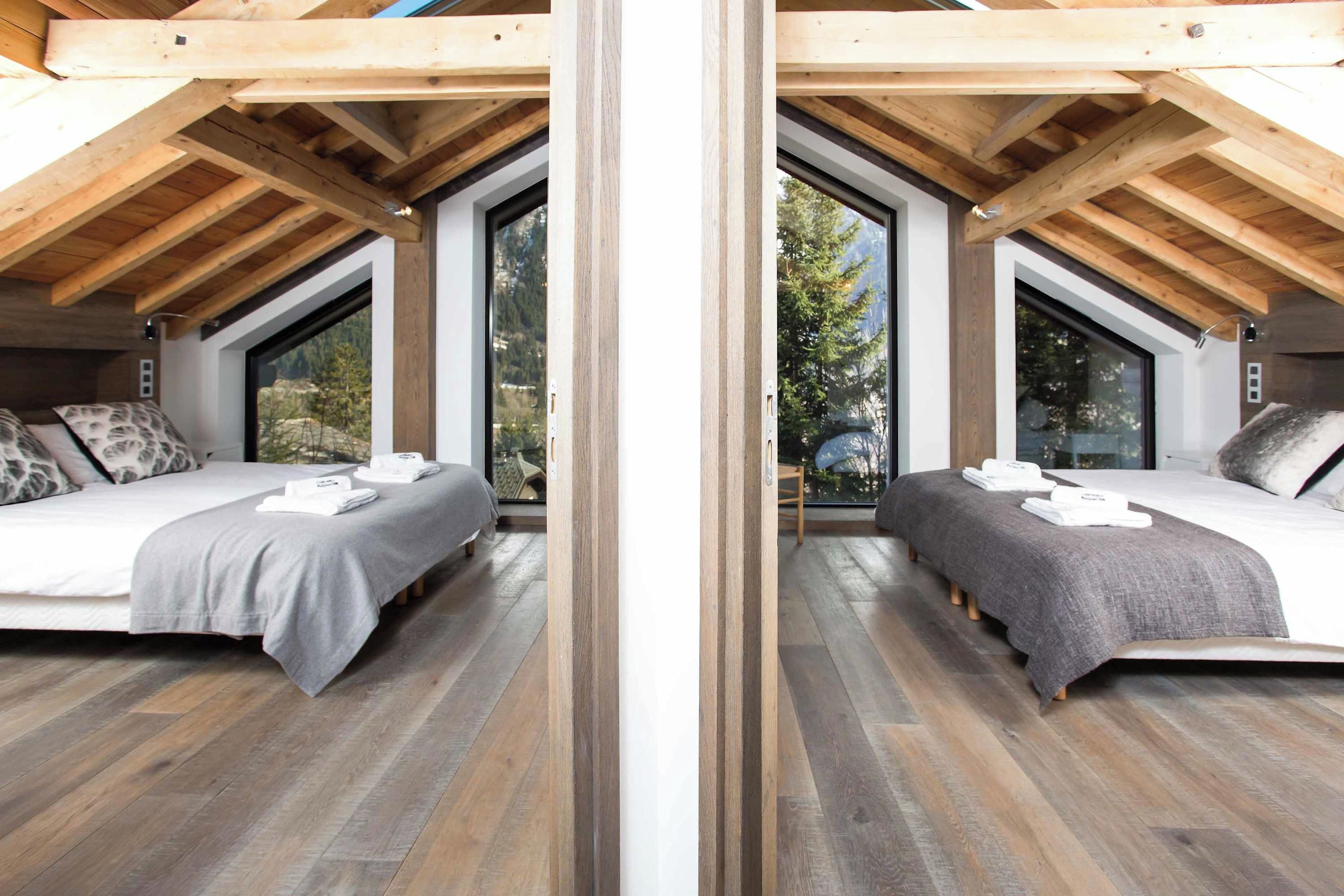 Une vue en miroir d’une chambre à coucher avec deux lits, un plancher en bois et de grandes fenêtres.