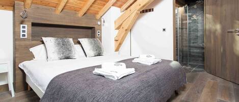 A bedroom with a wooden ceiling, a bed with a gray blanket, a white bedside table, and a wardrobe.