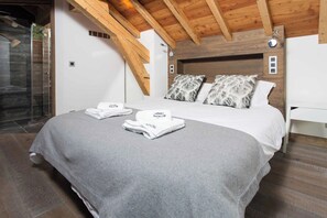 A bedroom with a wooden ceiling, a bed with white bedding, two pillows, and a pair of towels on the bed. - Ski Chalet La Source with hot tub (Chamonix)