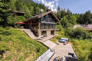 A modern two-story house with a deck, outdoor seating, and a hot tub.