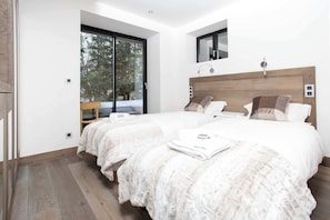 Un dormitorio moderno con dos camas, un ventanal grande y vistas a árboles.